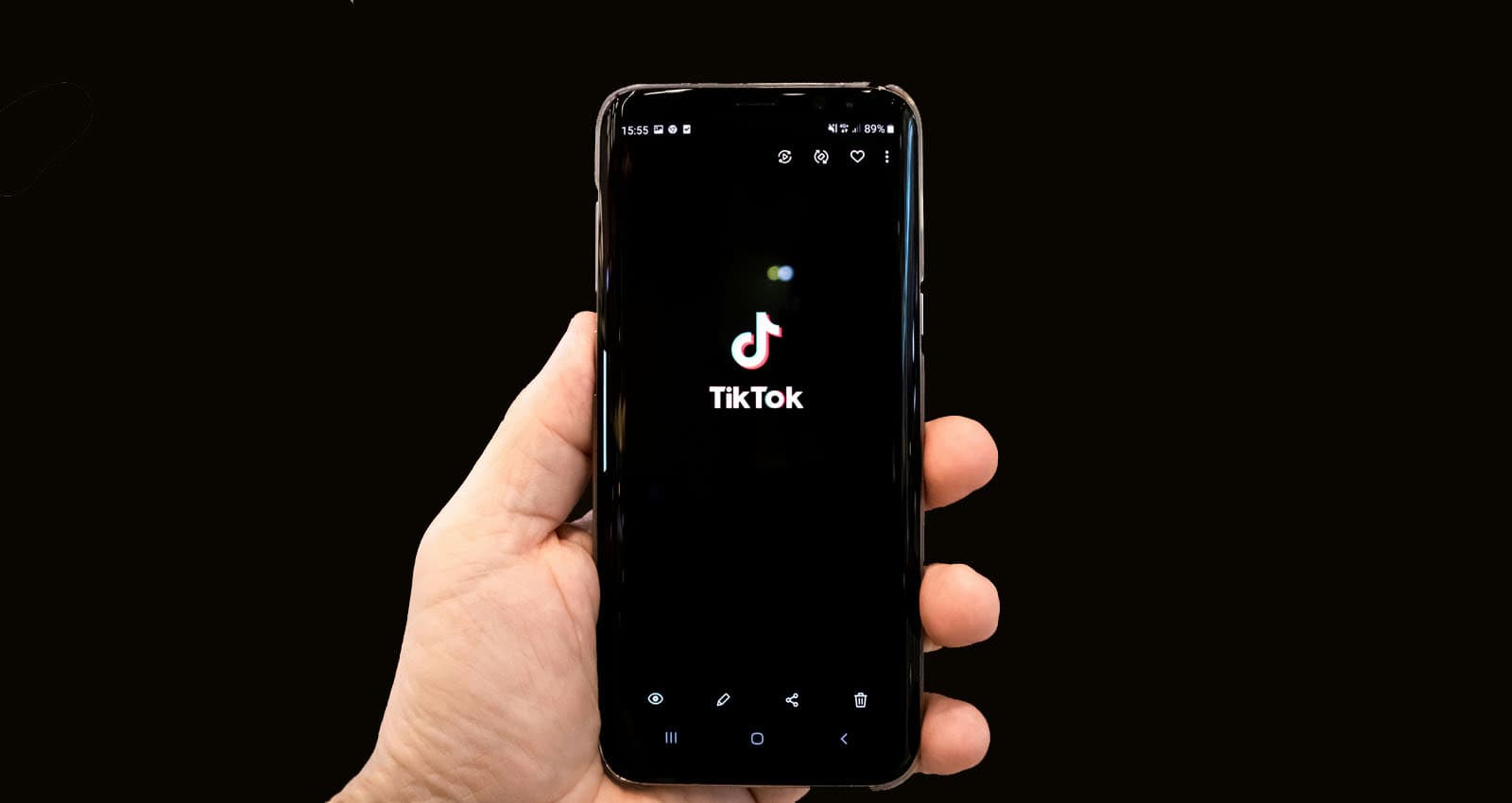 Black background with hand holding a smartphone that displays the TikTok logo.