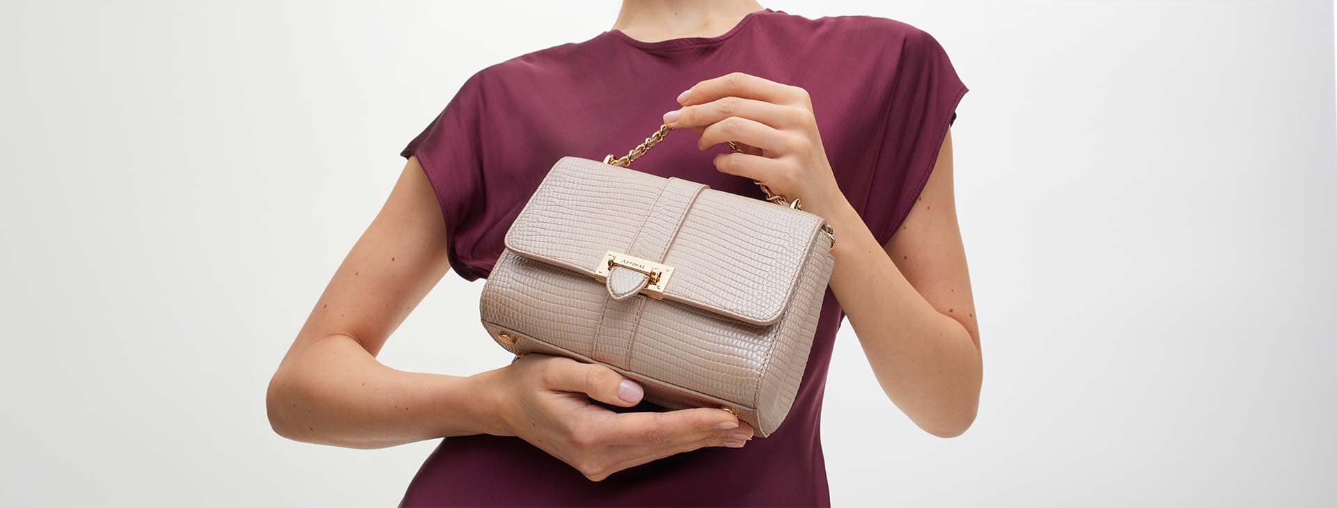 Female torso and arms in red top holding a beige Aspinal of London handbag.