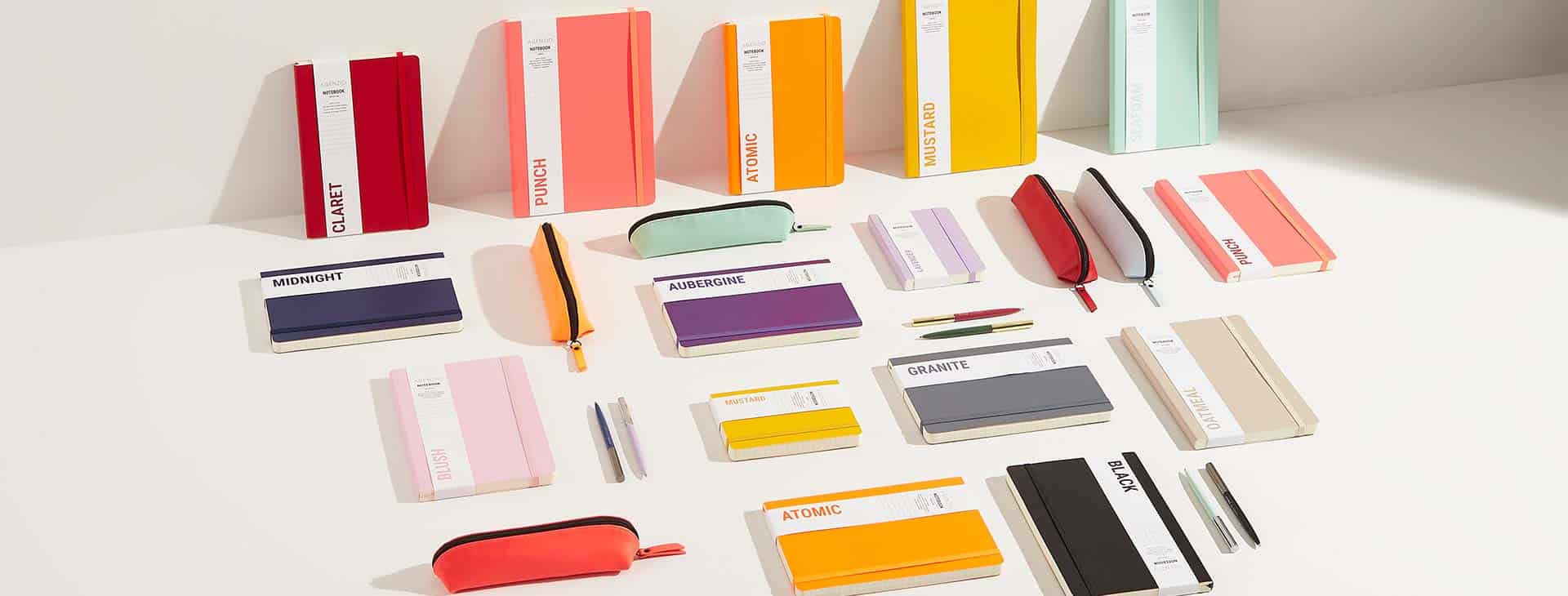 A white background with various coloured notebooks and pens.