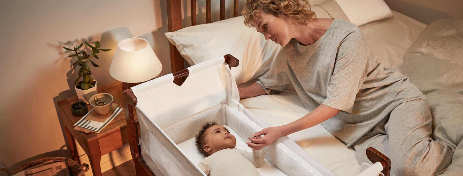 Mother led on bed looking at baby in a Snuz pod next to the bed.